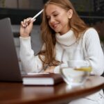 woman holding a pen looking at a laptop