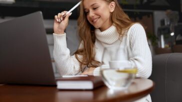 woman holding a pen looking at a laptop