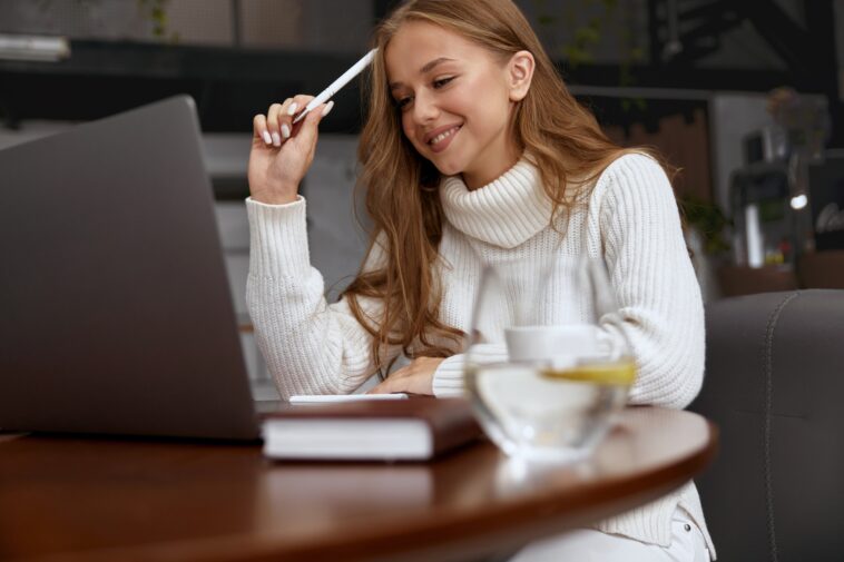 woman holding a pen looking at a laptop