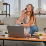 smiling woman with a headset sitting on a couch with a laptop in front of her