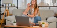 smiling woman with a headset sitting on a couch with a laptop in front of her