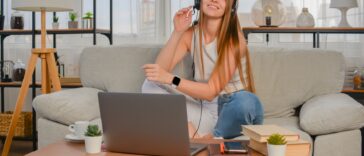 smiling woman with a headset sitting on a couch with a laptop in front of her