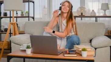 smiling woman with a headset sitting on a couch with a laptop in front of her