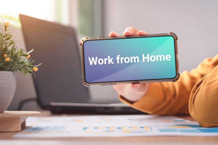 person holding a smartphone with a work from home message on the screen