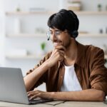 smiling man with glasses working on a laptop from home