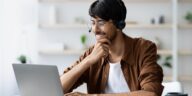 smiling man with glasses working on a laptop from home