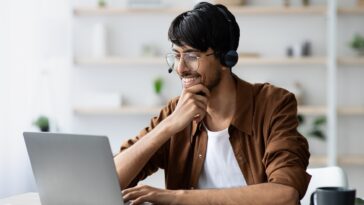 smiling man with glasses working on a laptop from home