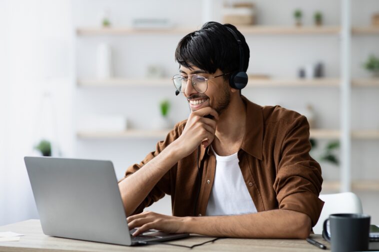 smiling man with glasses working on a laptop from home