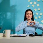 woman making a heart shaped sign sitting at a desk in a home office