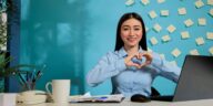 woman making a heart shaped sign sitting at a desk in a home office