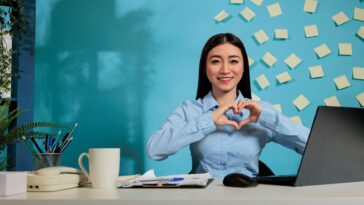 woman making a heart shaped sign sitting at a desk in a home office