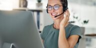 smiling woman with headset working on a computer from home