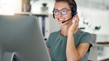 smiling woman with headset working on a computer from home