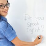 woman writing "Do you speak English?" on a white board