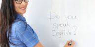 woman writing "Do you speak English?" on a white board