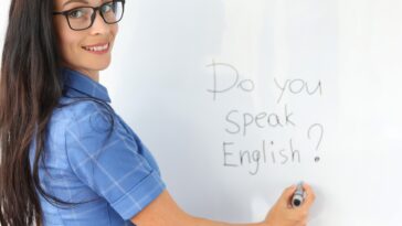 woman writing "Do you speak English?" on a white board