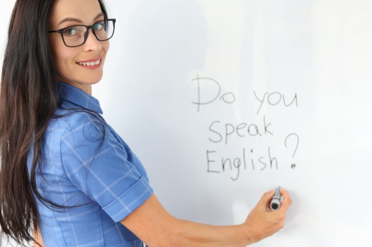 woman writing "Do you speak English?" on a white board