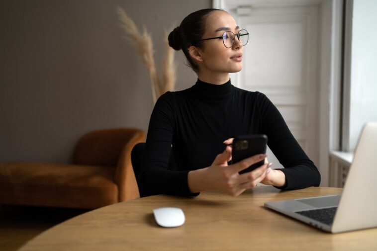woman with glasses working from home with a laptop and smartphone