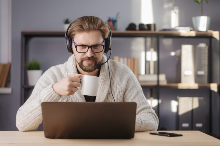 man holding a mug and working on a laptop at home