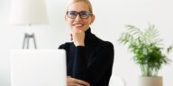 smiling woman with glasses sitting at a desk with a laptop