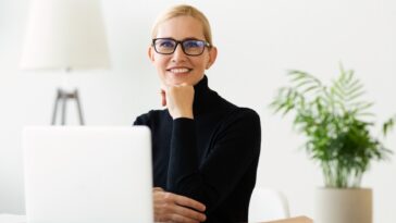 smiling woman with glasses sitting at a desk with a laptop