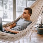 man working on a laptop while laying in a hammock at home