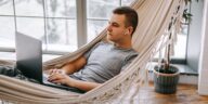 man working on a laptop while laying in a hammock at home