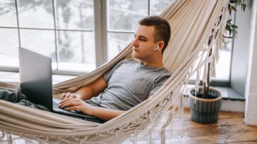 man working on a laptop while laying in a hammock at home