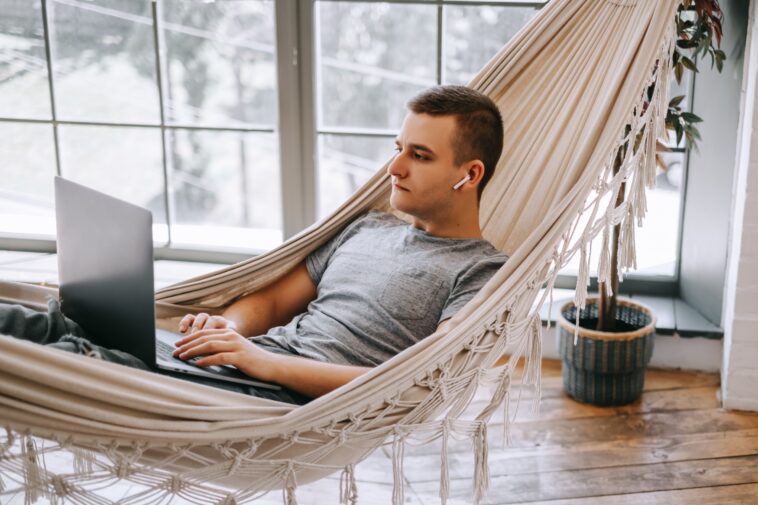 man working on a laptop while laying in a hammock at home