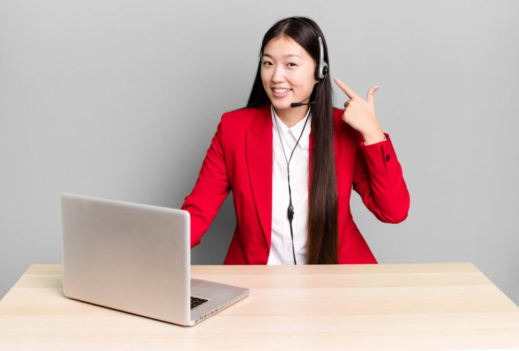 woman sitting behind a desk with a laptop pointing at her headset