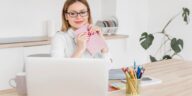 woman sitting at a desk, holding a notebook and looking at a laptop