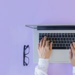 hands on a laptop with glasses next to it