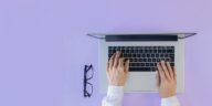 hands on a laptop with glasses next to it