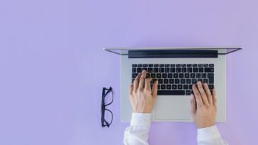 hands on a laptop with glasses next to it