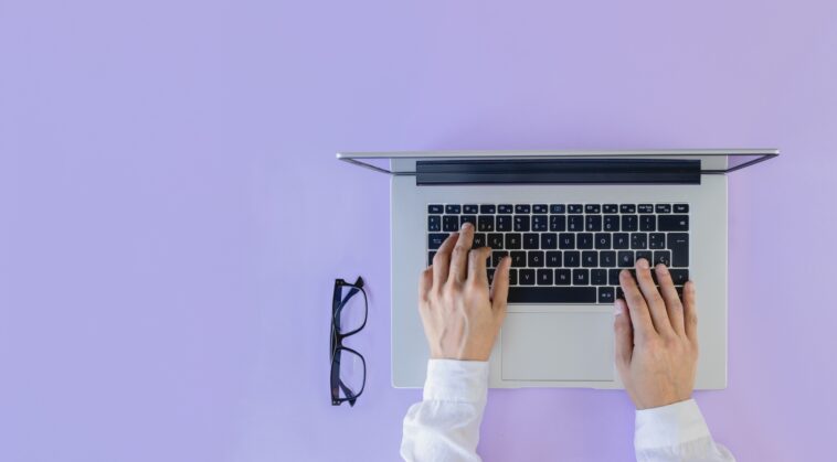hands on a laptop with glasses next to it