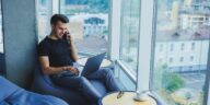 man sitting in a modern home office using a laptop and talking on a phone