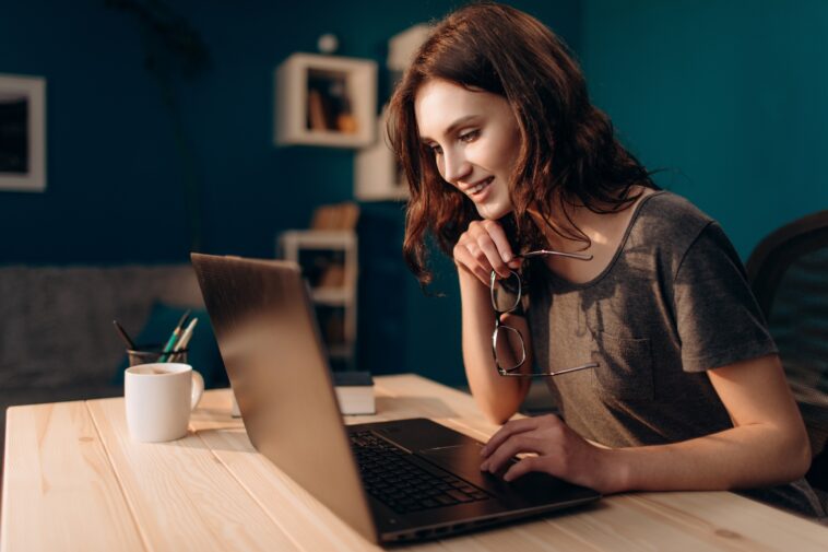 woman working on a laptop from home holding glasses