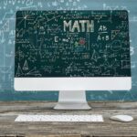 computer screen in front of a blackboard with mathematical formulas on them