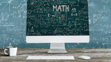 computer screen in front of a blackboard with mathematical formulas on them