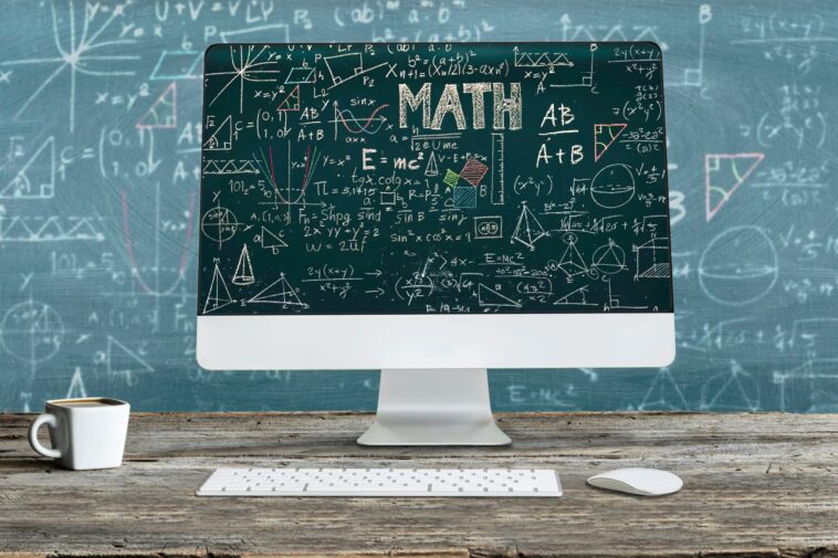 computer screen in front of a blackboard with mathematical formulas on them