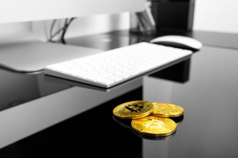 3 gold bitcoins on a black table next to a white computer