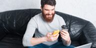 man sitting on a sofa using a smartphone and holding a coffee cup