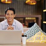 smiley man sitting on a couch with a laptop and coffee cup in front of him