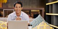 smiley man sitting on a couch with a laptop and coffee cup in front of him