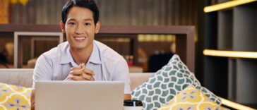 smiley man sitting on a couch with a laptop and coffee cup in front of him