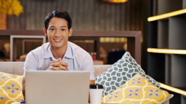 smiley man sitting on a couch with a laptop and coffee cup in front of him