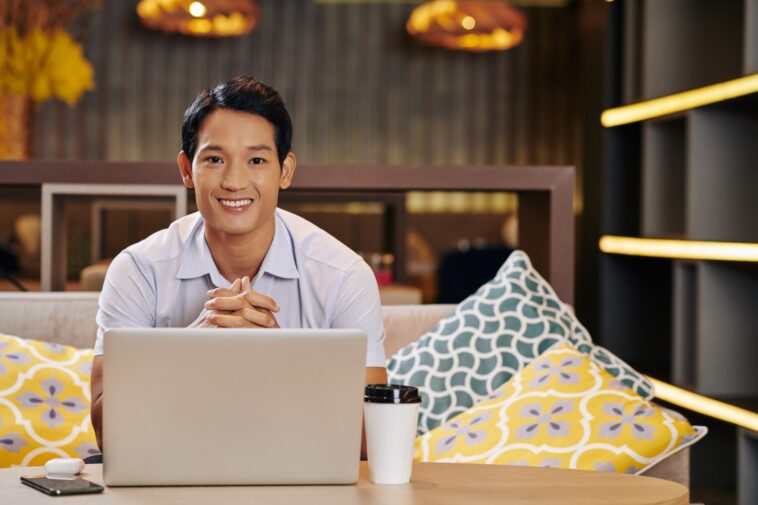 smiley man sitting on a couch with a laptop and coffee cup in front of him