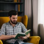 man sitting in a yellow chair reading a book