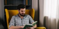 man sitting in a yellow chair reading a book