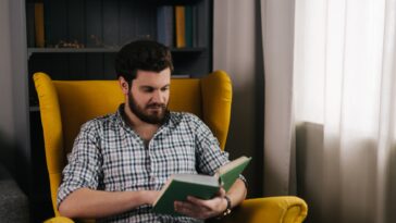 man sitting in a yellow chair reading a book